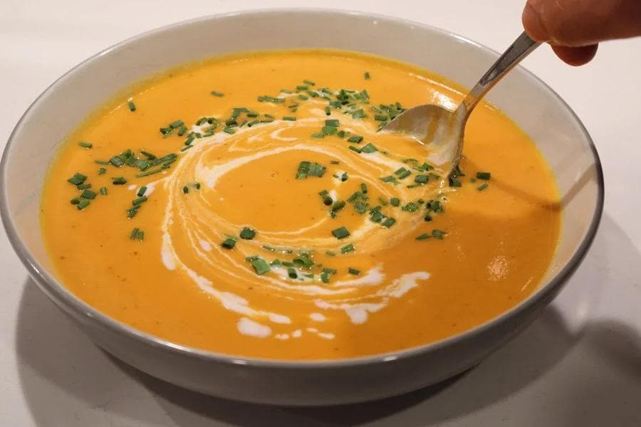 Creamy carrot and ginger soup garnished with fresh chives and a swirl of coconut cream.