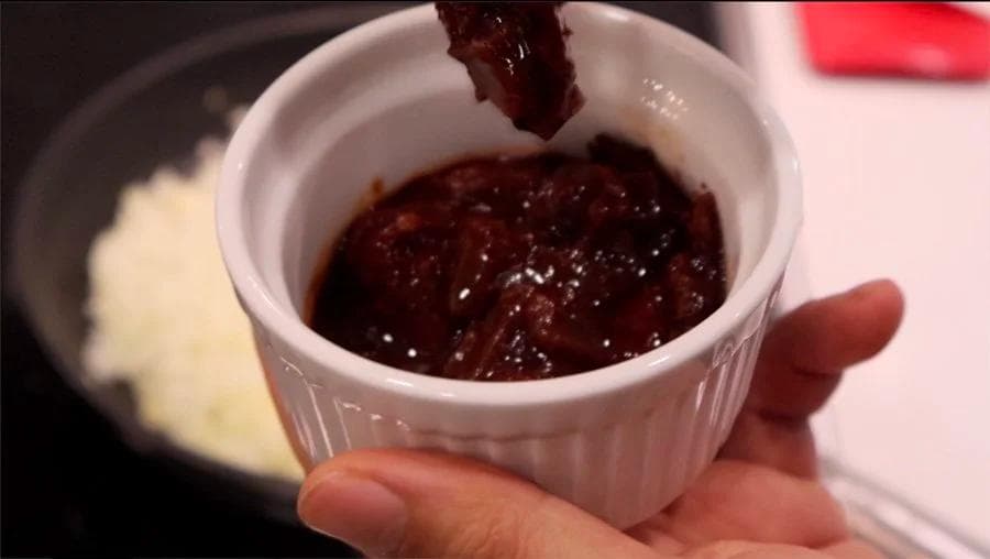 Dark red chipotle pepper mixture being drizzled into a white bowl during meatloaf ingredient preparation.