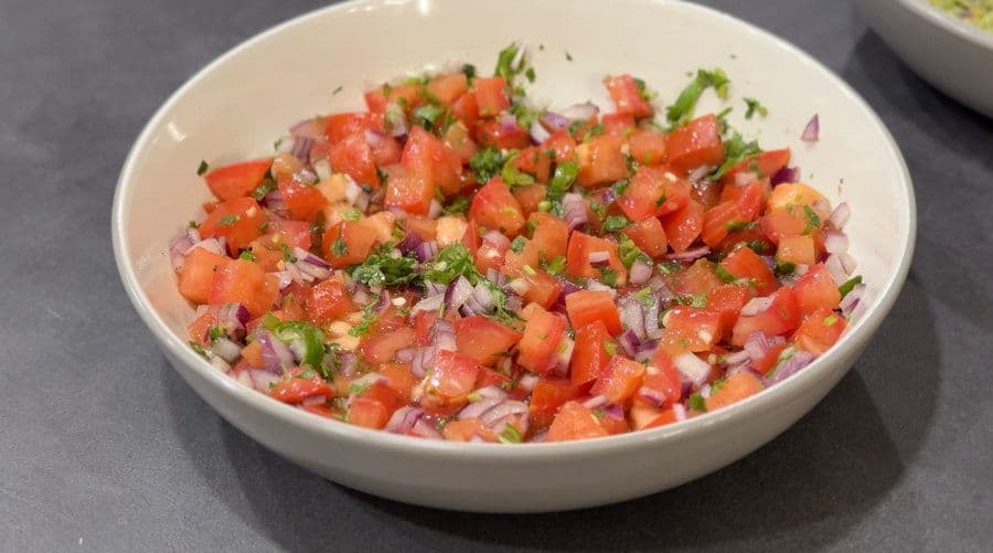Freshly made pico de gallo in a white bowl, showing diced tomatoes, red onions, and cilantro mixed together.