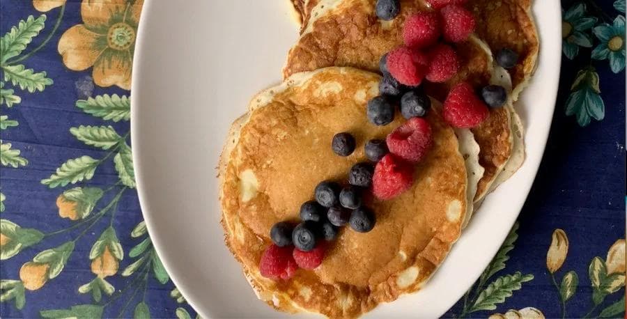 Stack of golden buttermilk pancakes topped with fresh raspberries and blueberries on a white plate.