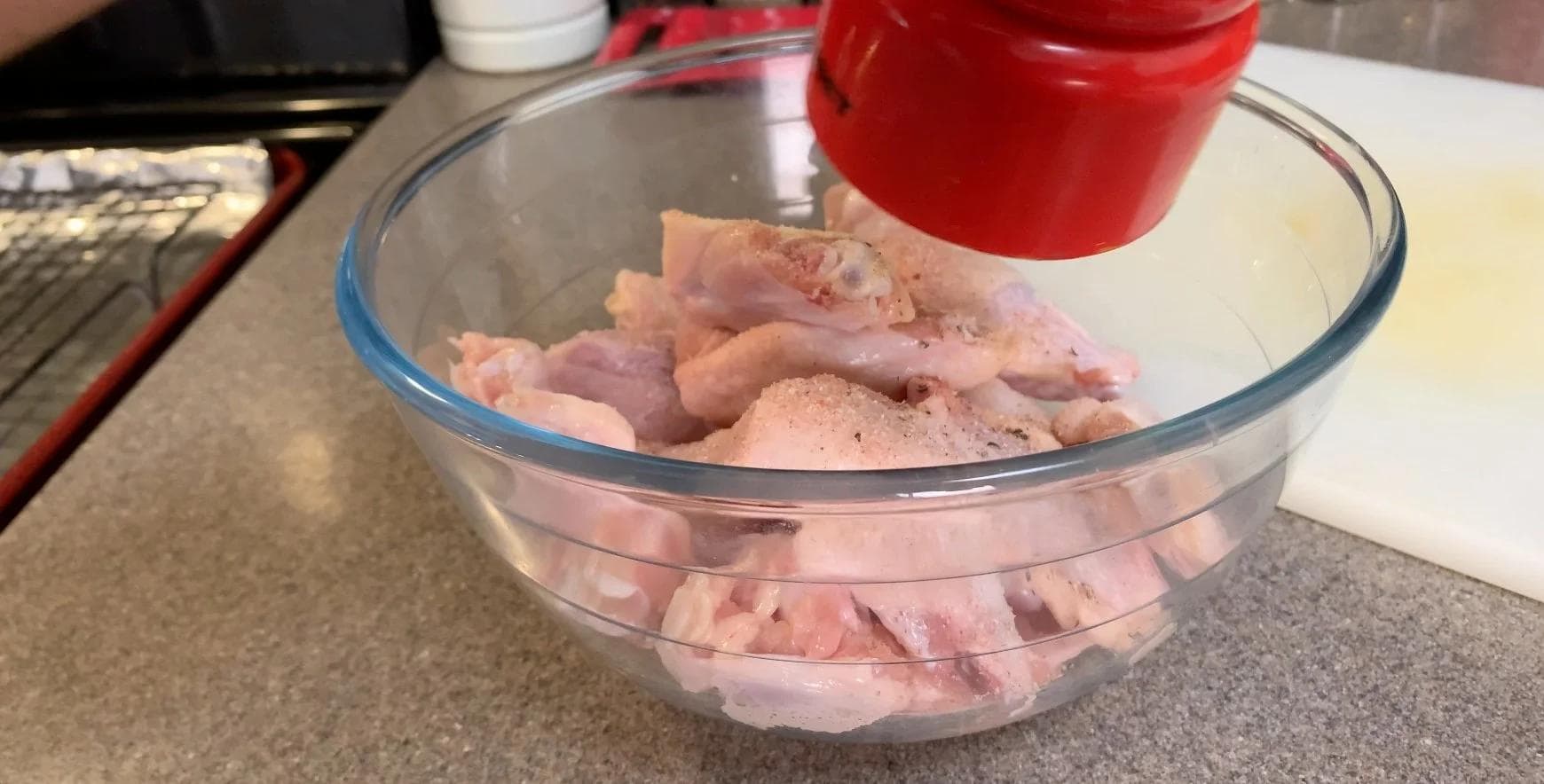 Seasoned raw chicken wings coated with flour and spices in a glass bowl before air frying.