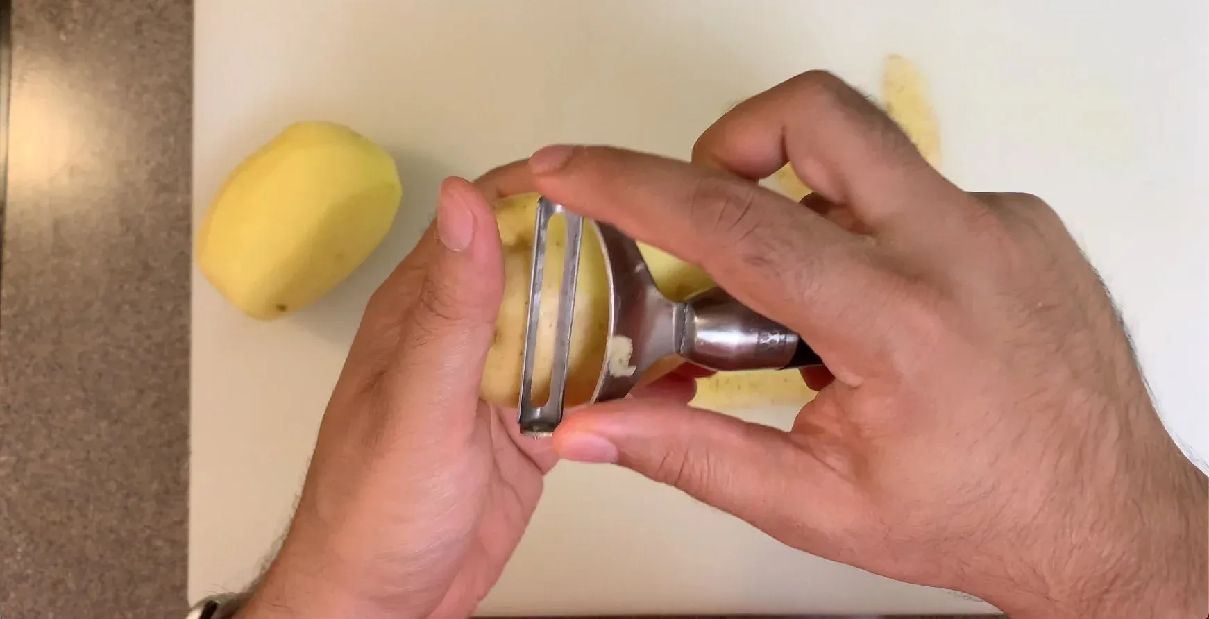 Hands using a crinkle cutter to slice a potato lengthwise into waffle fries.
