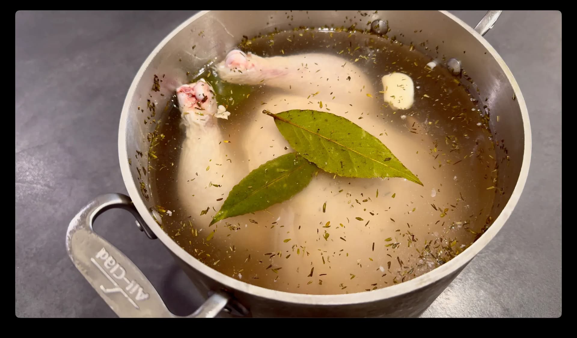 Whole chicken brining in salted water with bay leaves and garlic in a large pot