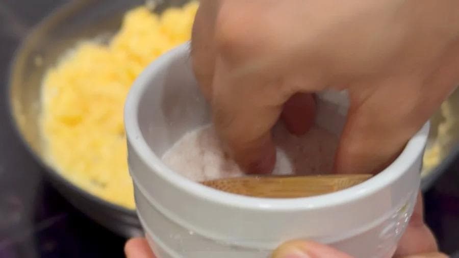 Hand dipping wooden spoon into white bowl of scrambled eggs during breakfast burrito preparation.