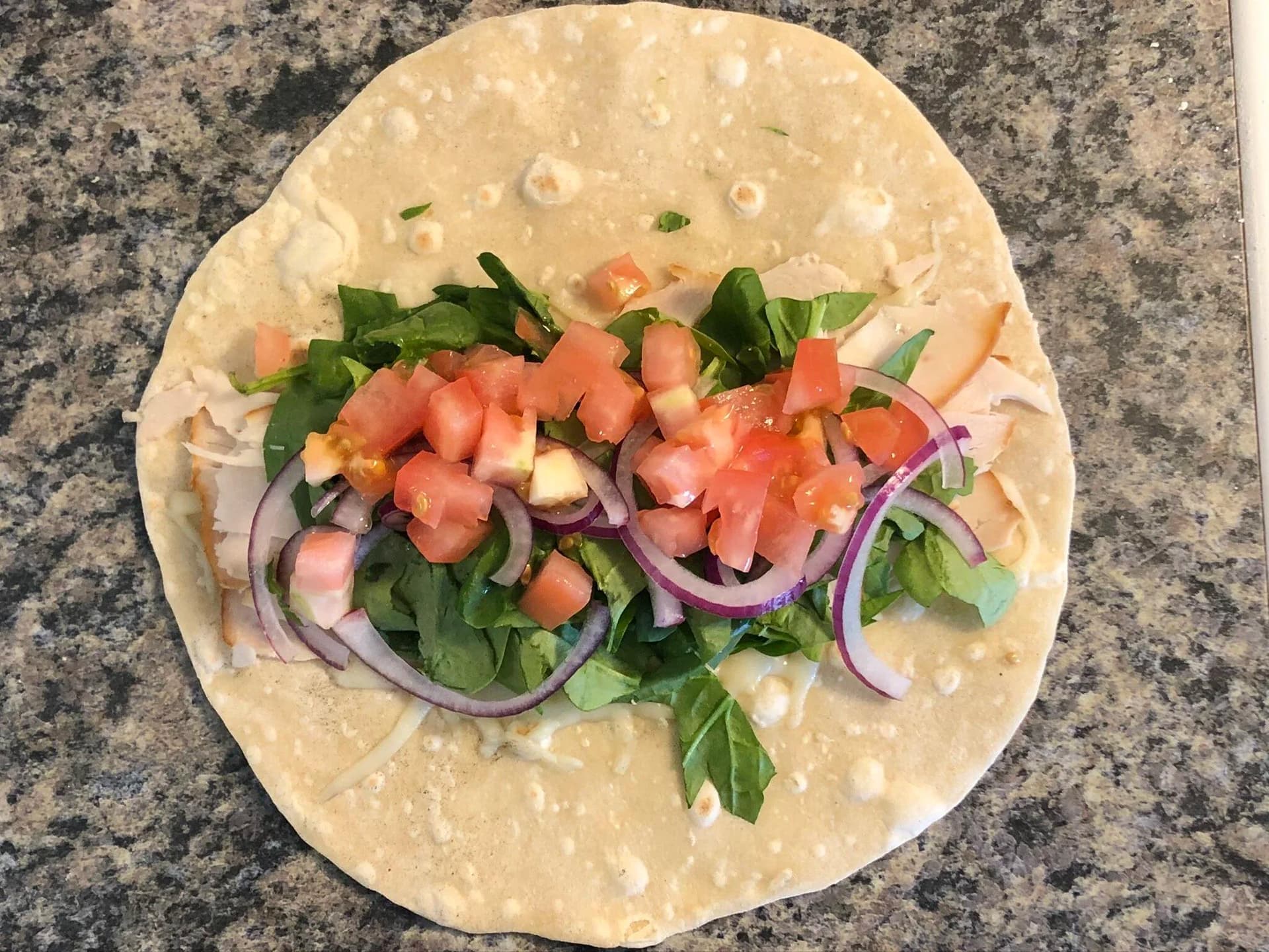 Turkey wrap with sliced purple onions, chopped tomatoes, and fresh greens on a flour tortilla.