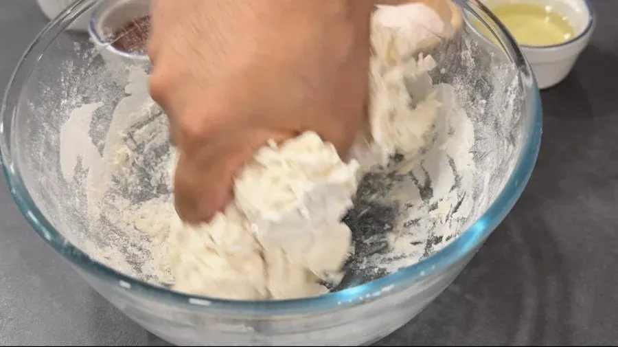 Hand mixing flour and hot water dough in a glass bowl with chopsticks