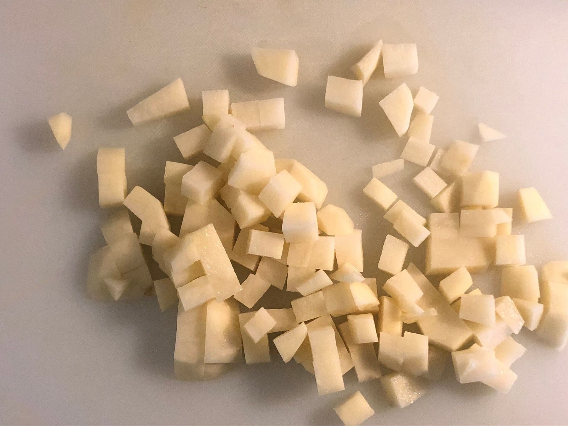 Diced potatoes on a white surface, ready to be rinsed and cooked for poha.