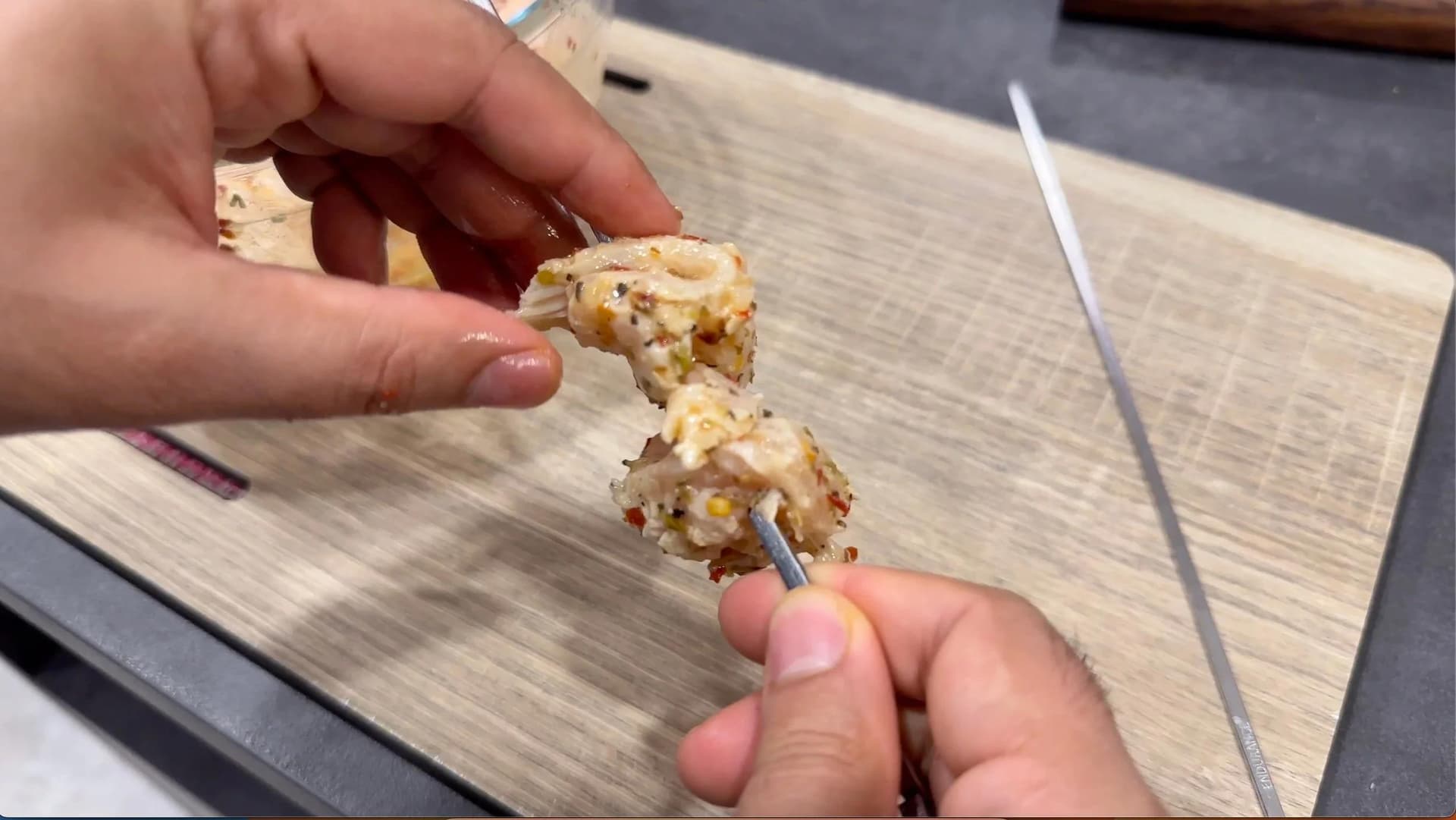 Marinated chicken cubes threaded onto a metal skewer, held over a wooden cutting board.