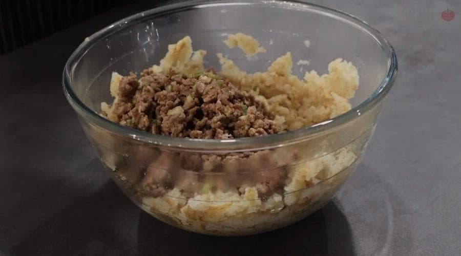Mashed potatoes mixed with cooked ground meat in a glass bowl during Perkedel Daging preparation.
