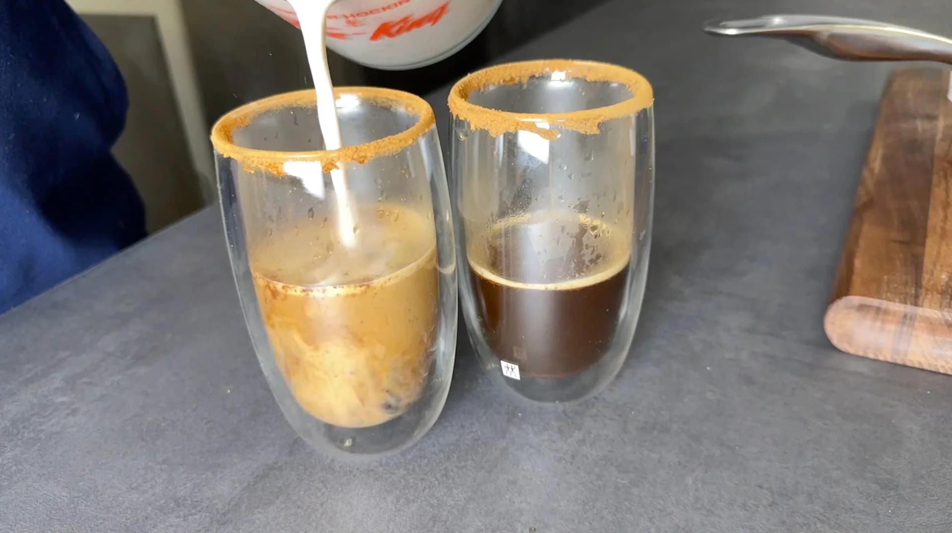Two double-wall glasses with gold-rimmed rims filled with coffee and steamed milk mixture, one lighter and one darker in color.