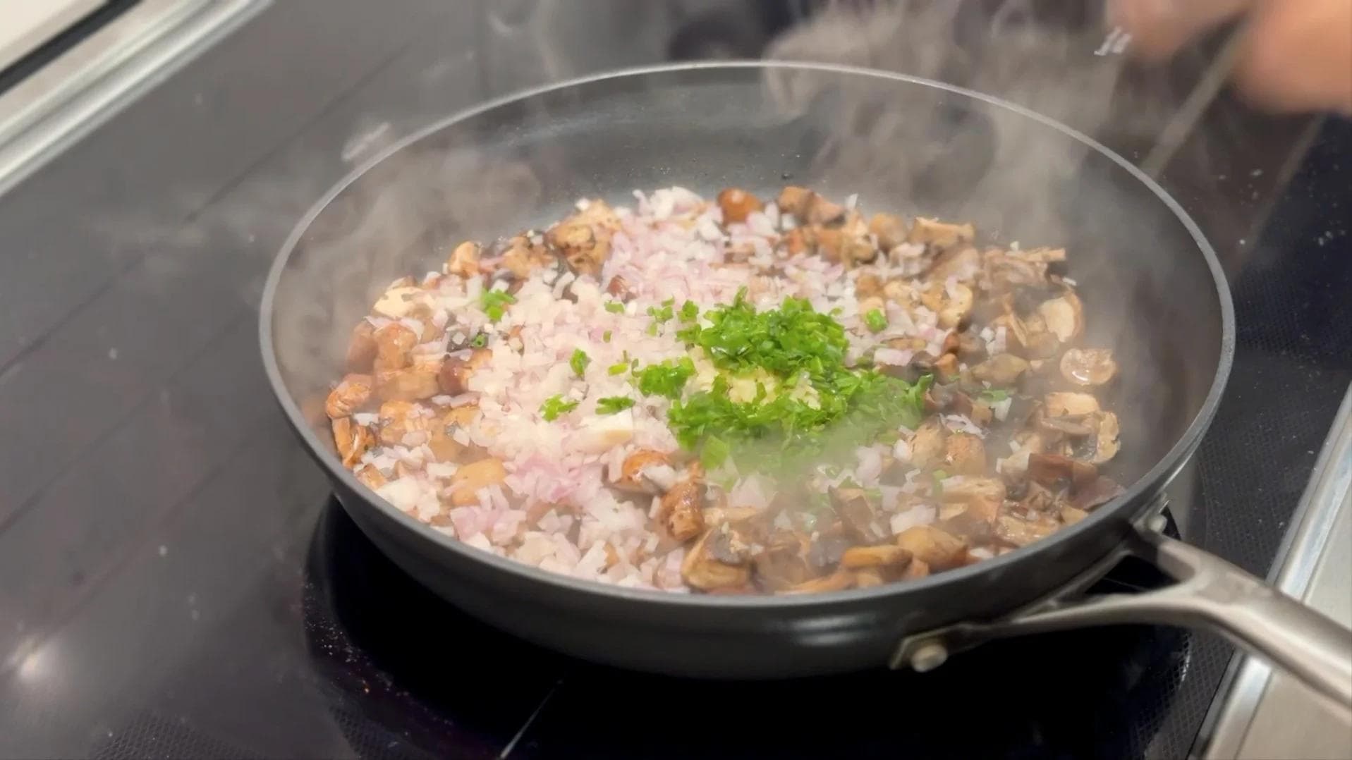 Sautéed mushrooms with diced shallots and fresh chives in a dark pan on stovetop