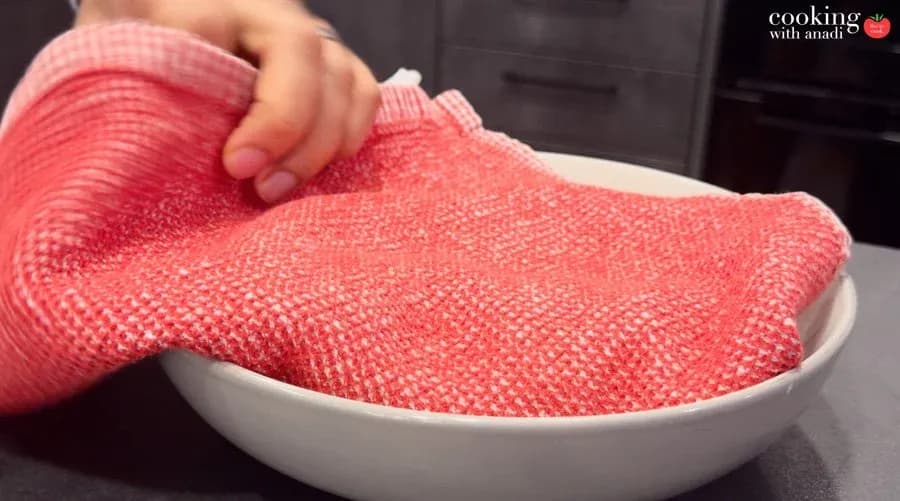 Warm tortillas covered with a red kitchen towel in a white bowl to keep them soft and pliable.
