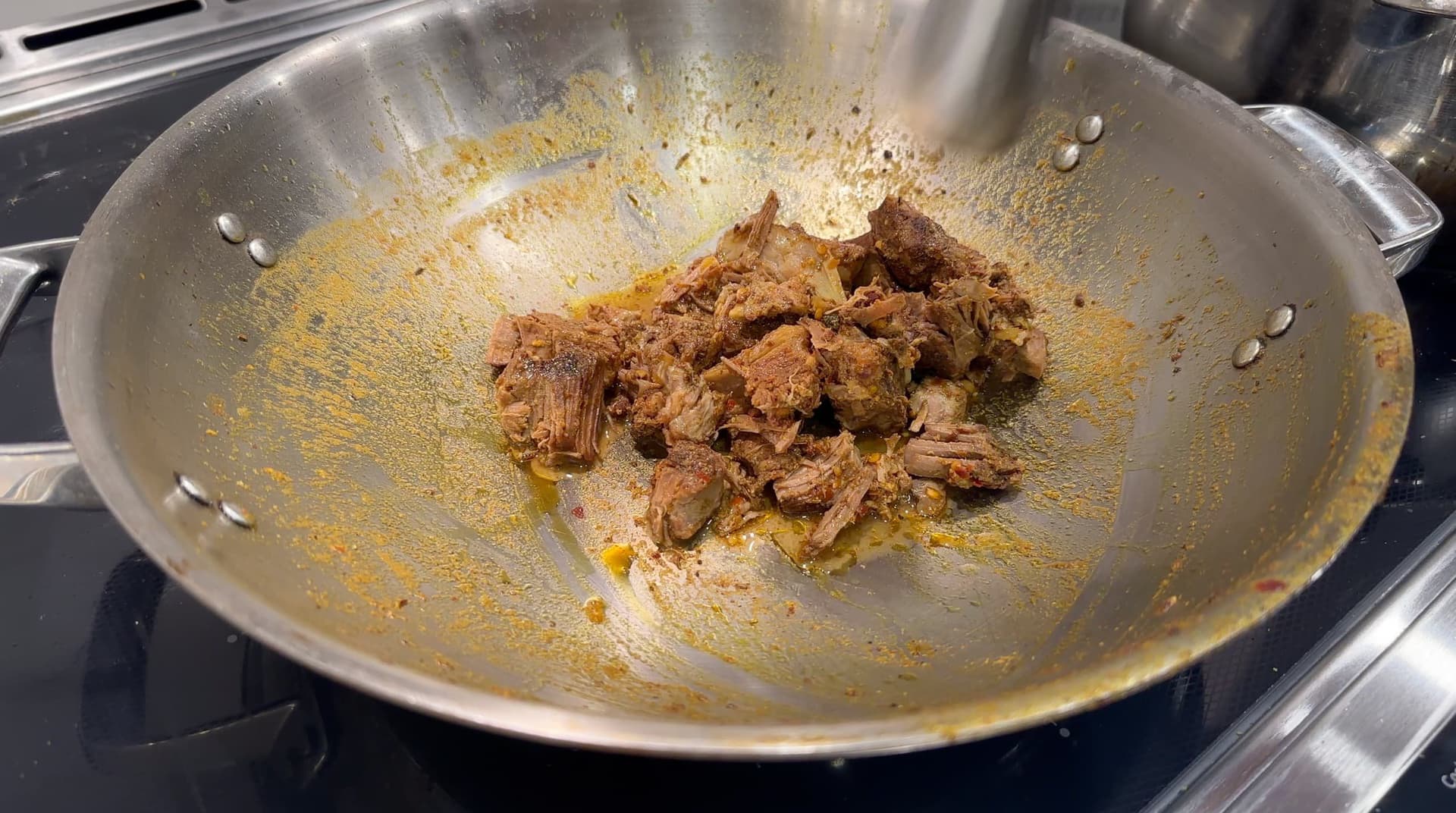 Shredded cooked lamb meat in a wok with golden spices and oil during preparation of haleem.