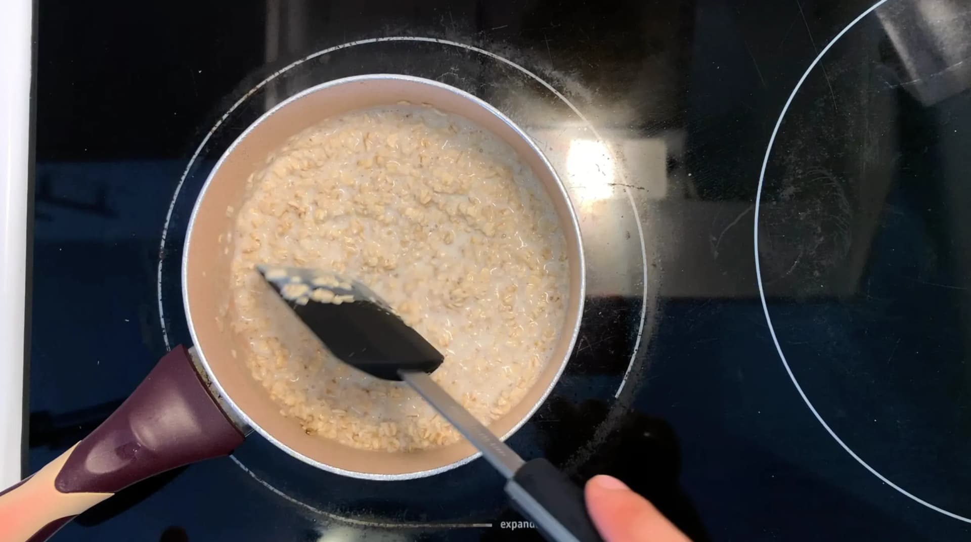 Stirring creamy oatmeal mixture in a saucepan with a spatula during cooking preparation.