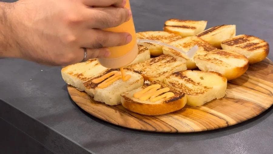 Toasted bread slices with butter and cinnamon arranged on a wooden cutting board, hand applying sauce.