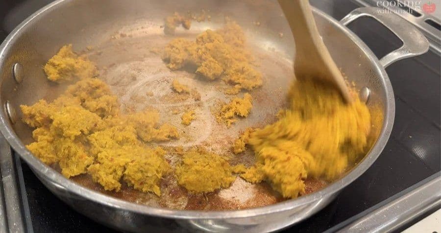 Blended yellow spice paste being stirred into a pan during the cooking process for beef rendang.