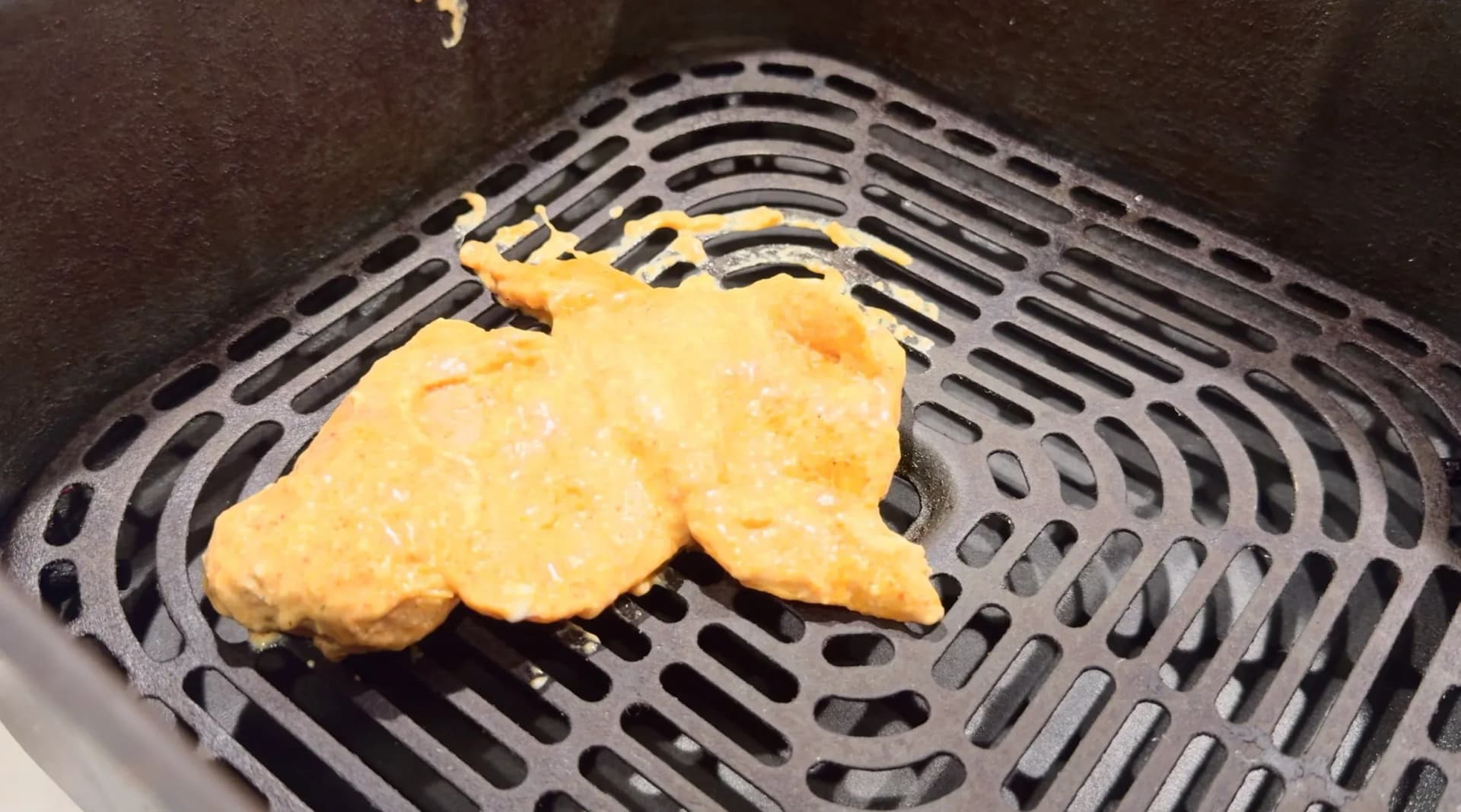 Single piece of marinated chicken tikka in an orange-red spiced coating placed in an air fryer basket