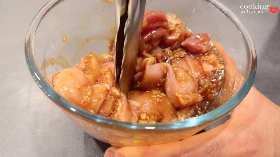 Raw chicken pieces coated in a dark marinade being tossed with tongs in a glass bowl.