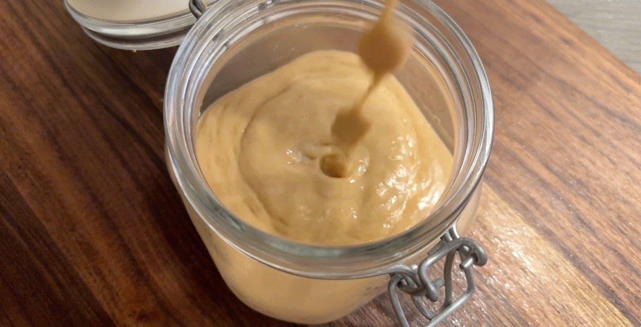 Homemade lactose-free condensed milk in a glass jar, showing thick, creamy beige mixture with a spoon.