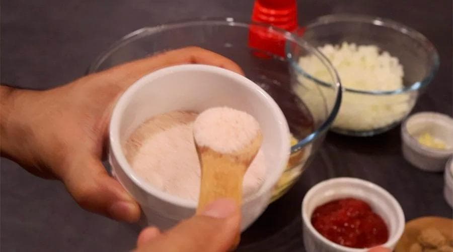 Hand mixing ground beef and breadcrumb mixture in a white bowl with other ingredients visible nearby.