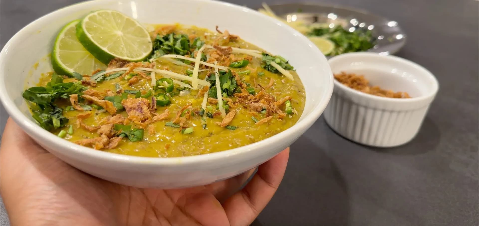 Bowl of Pakistani lamb haleem garnished with lime wedge, fresh herbs, and crispy fried onions.