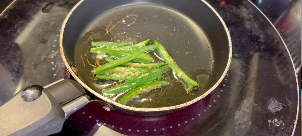 Green chillies sizzling in ghee in a pan during garnish preparation for Chicken Changezi.