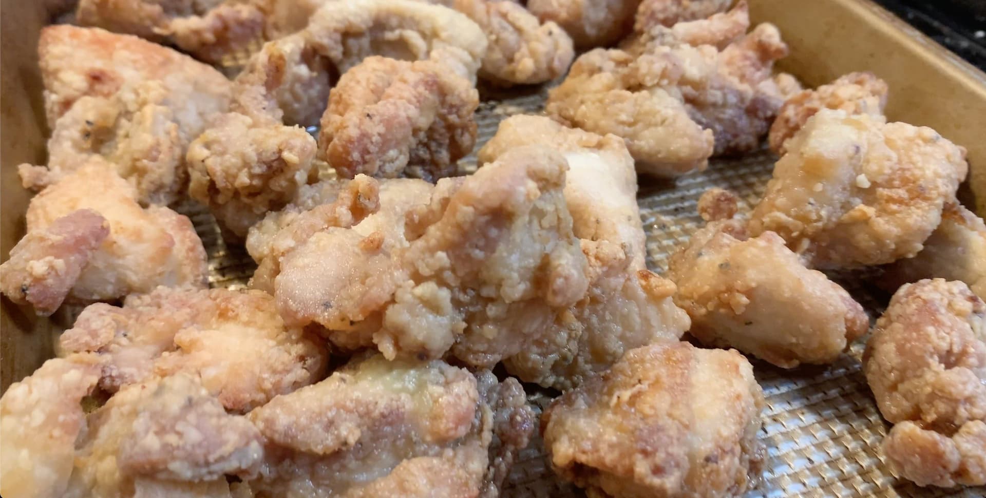 Crispy golden-brown Korean popcorn chicken pieces in a paper-lined box, showing the double-fried texture and rich coloring.
