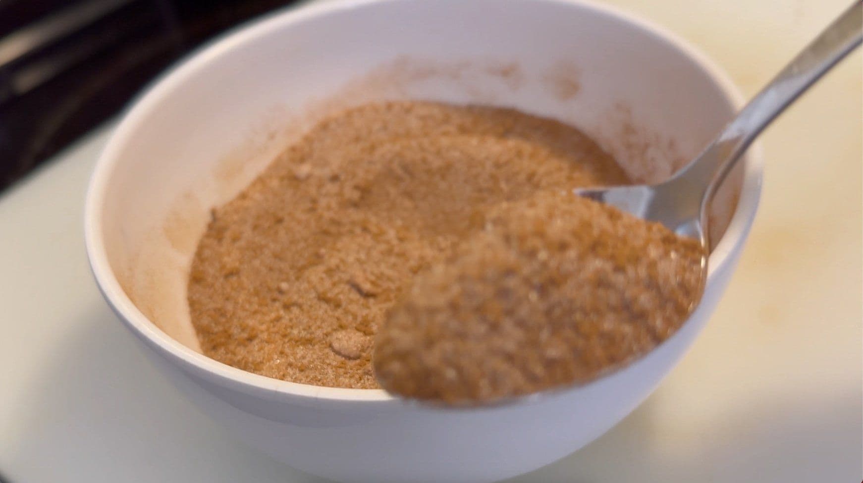 Cinnamon sugar mixture in white bowl with spoon, showing combined cinnamon, white sugar, and brown sugar.