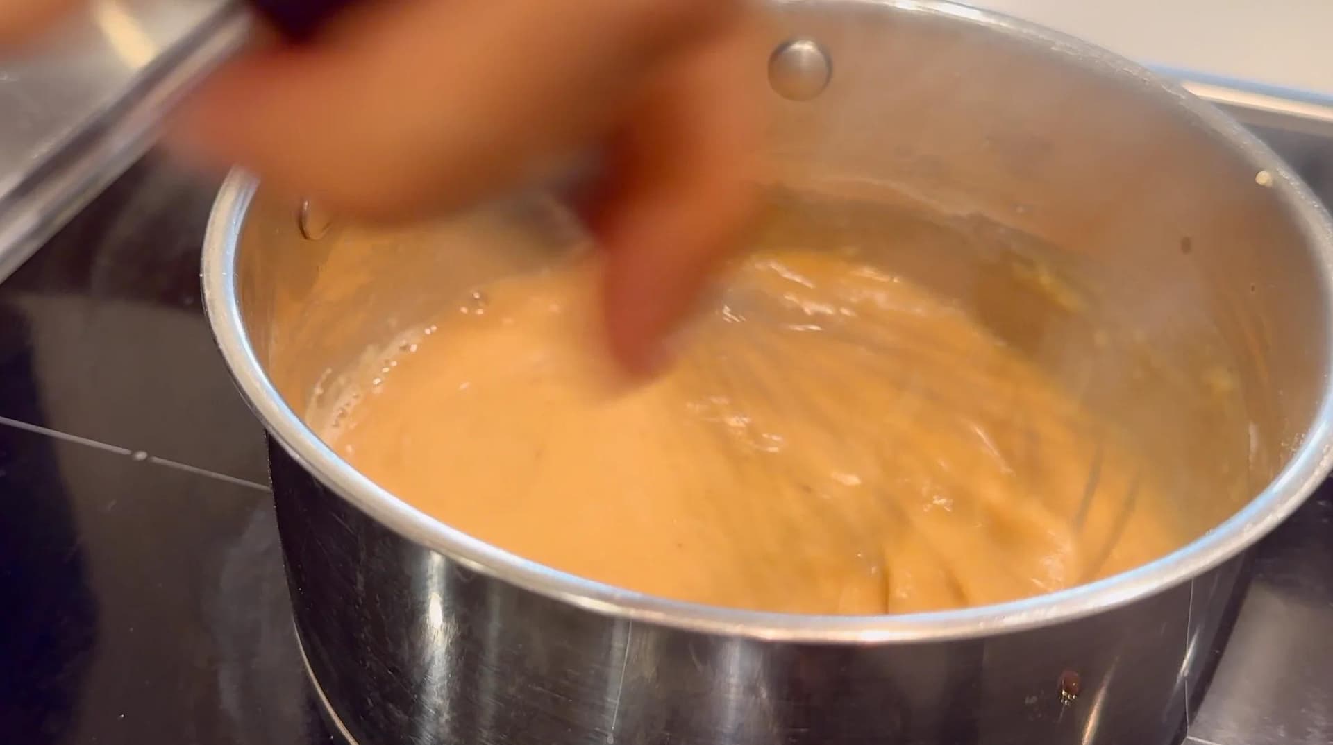 Whisking a golden-brown gravy in a stainless steel saucepan on the stovetop.