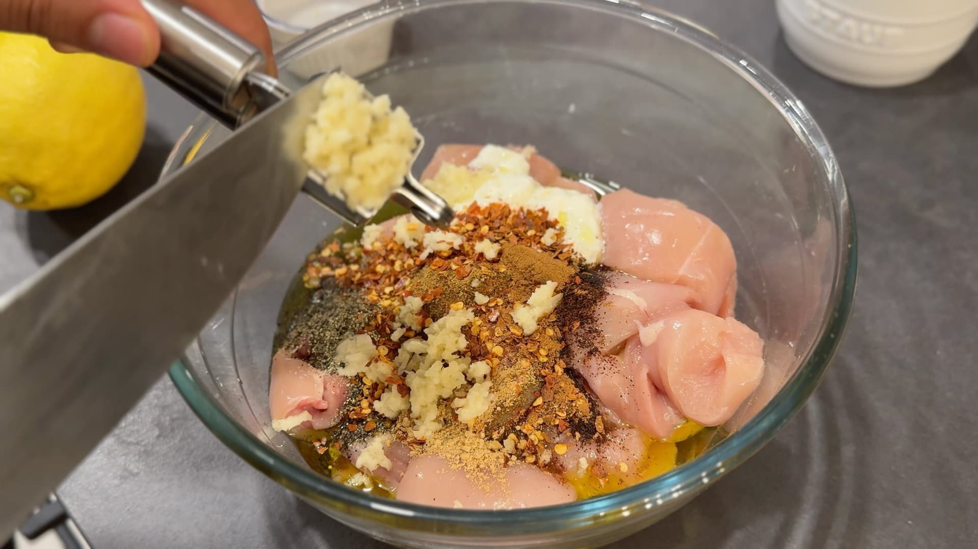 Chicken pieces marinated in yogurt, olive oil, spices, and minced garlic in a glass bowl.