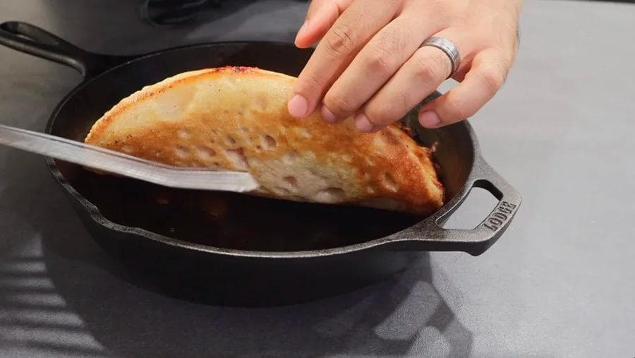 Crispy golden cast iron pan pizza being lifted with a spatula, showing caramelized cheese edges.