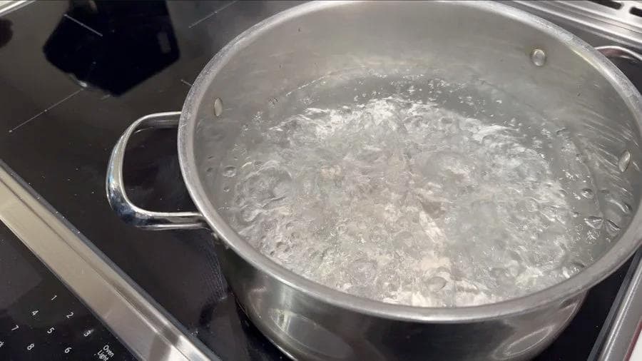 Boiling water with spinach leaves in a stainless steel pot on the stovetop.