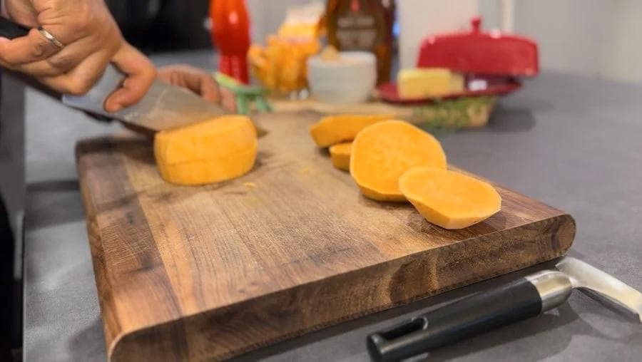 Sweet potatoes being sliced into rounds on a wooden cutting board during preparation.