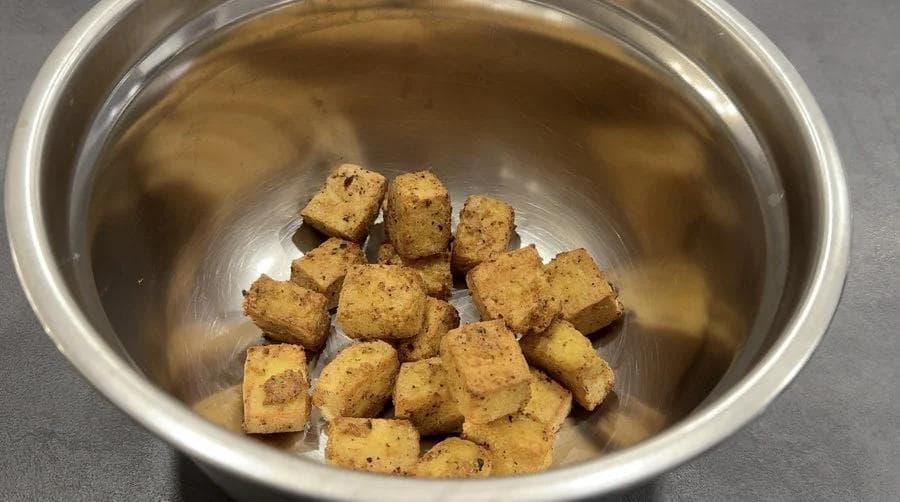 Crispy golden tofu cubes in a stainless steel bowl ready to be coated with sauce.