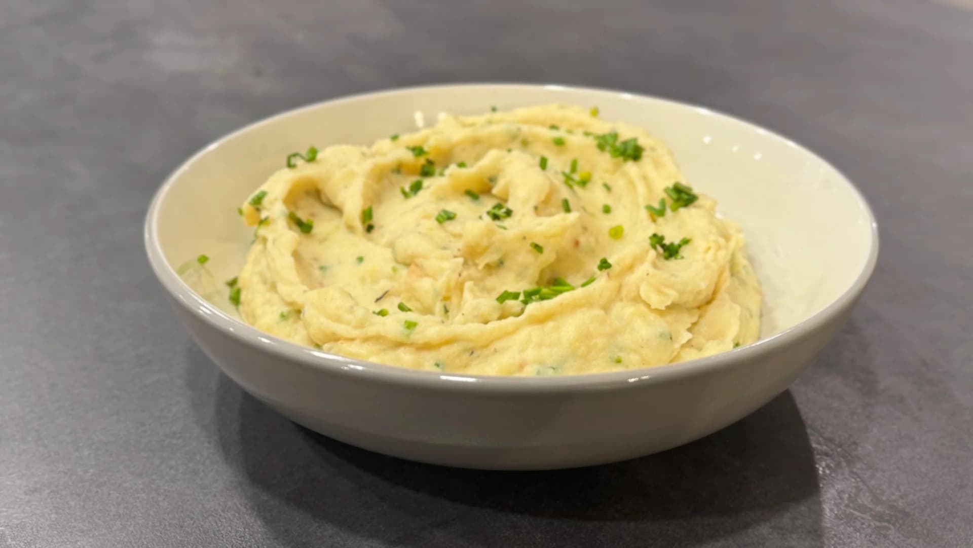 Creamy buttery garlic-herb mashed potatoes garnished with fresh chives in a white bowl.