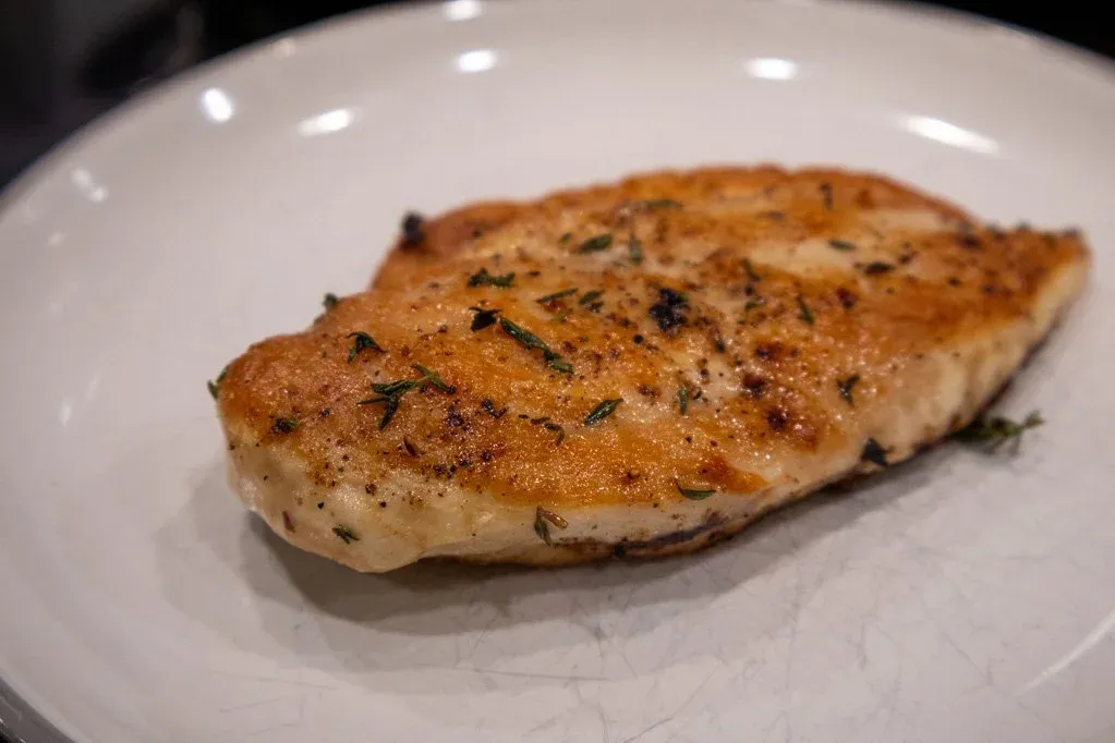 Pan-seared chicken breast with garlic and thyme seasoning on a white plate