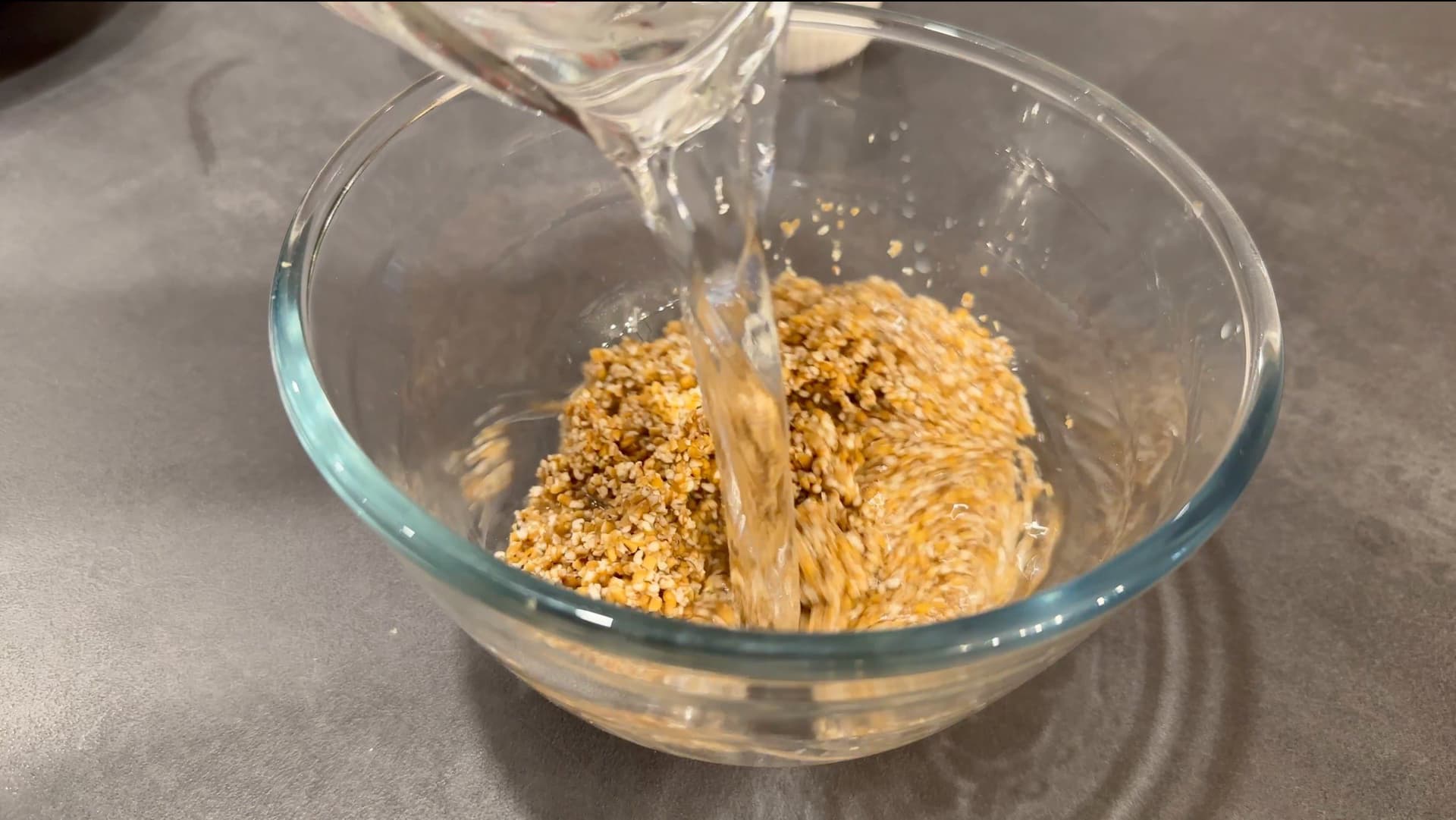 Water being poured into a glass bowl containing soaked lentils and rice for Pakistani haleem.