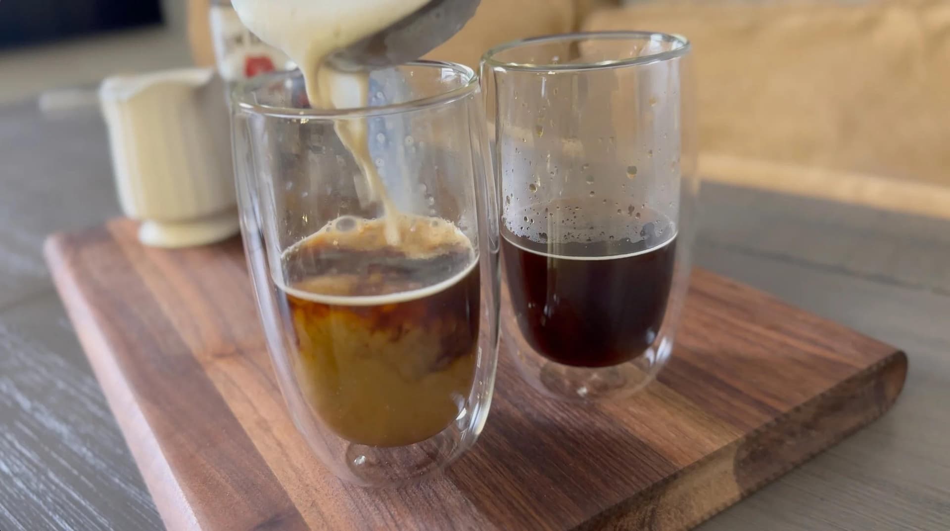 Two glasses of coffee at different stages of preparation on a wooden board, demonstrating the espresso and full drink comparison.