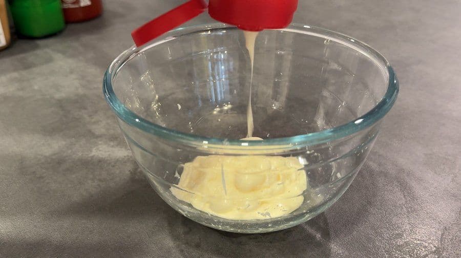 Creamy yellow umami sauce mixed in a clear glass bowl with a red spatula on gray countertop