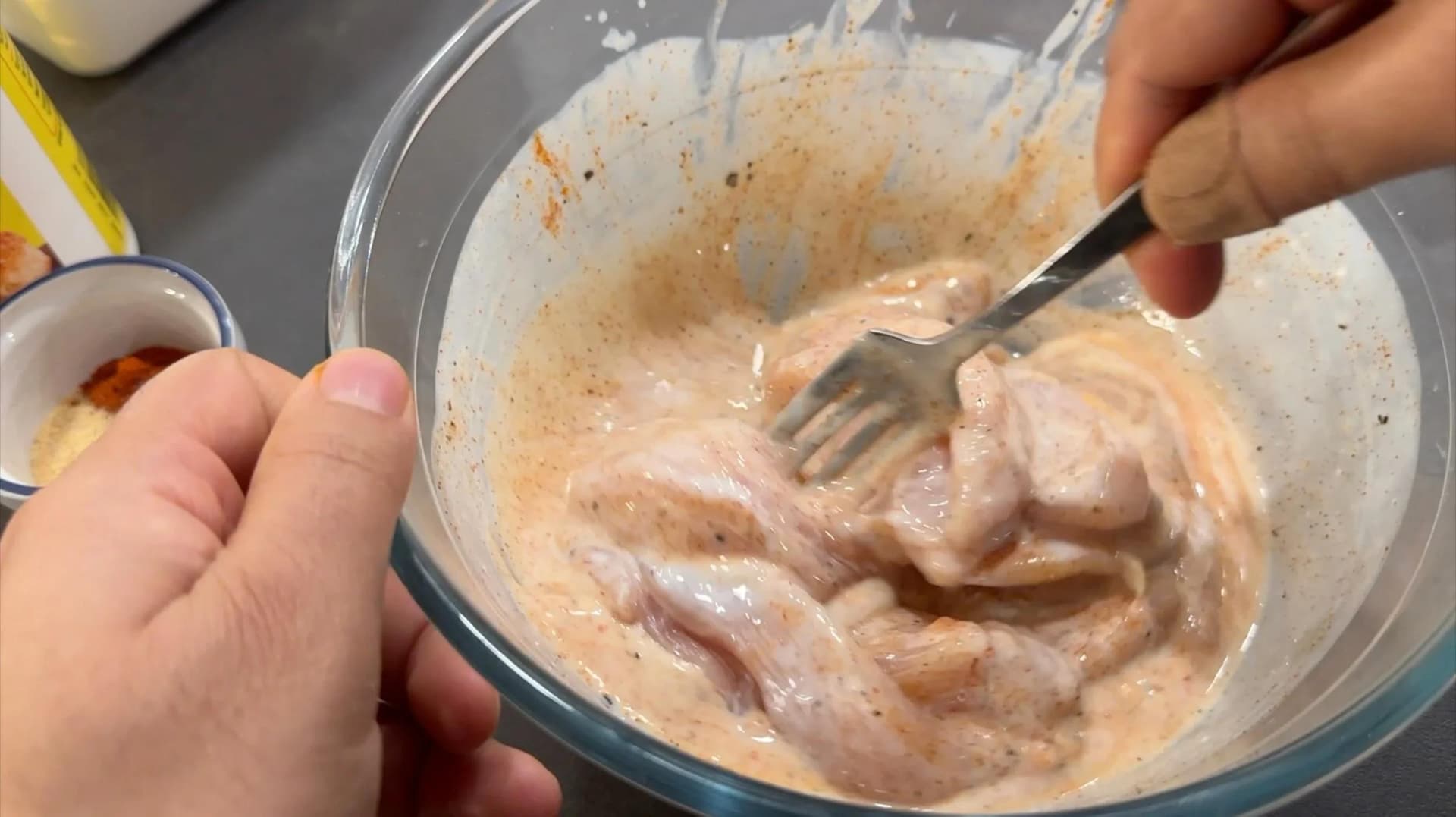 Chicken tenders being tossed in buttermilk marinade with a fork in a glass bowl.
