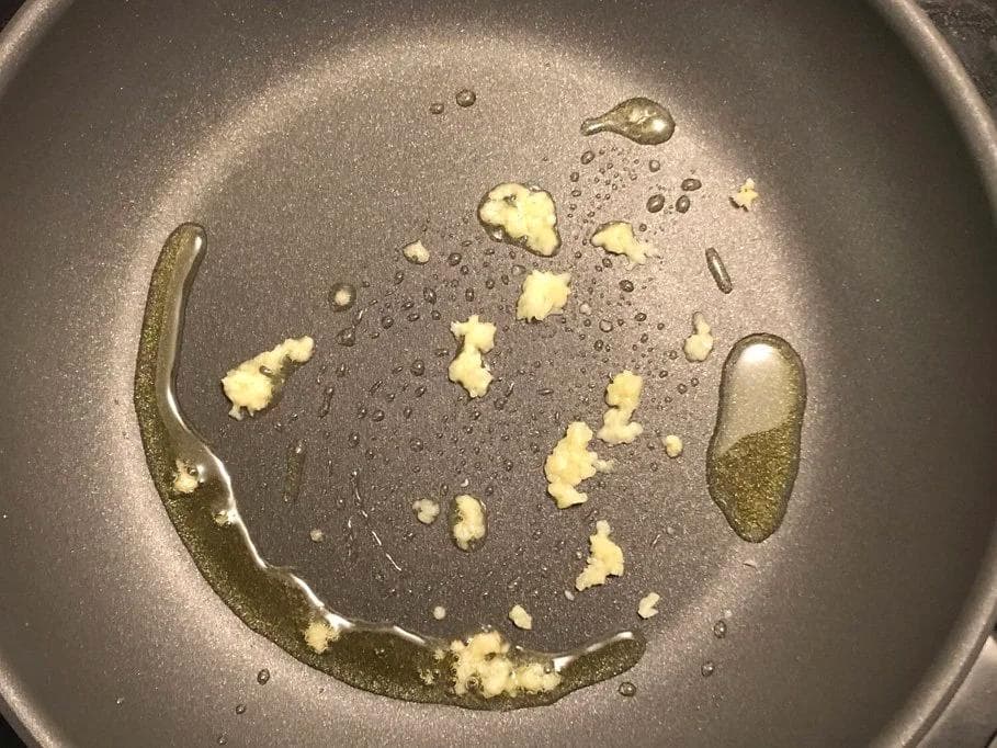 Green beans and minced garlic cooking in olive oil in a dark skillet over medium heat.