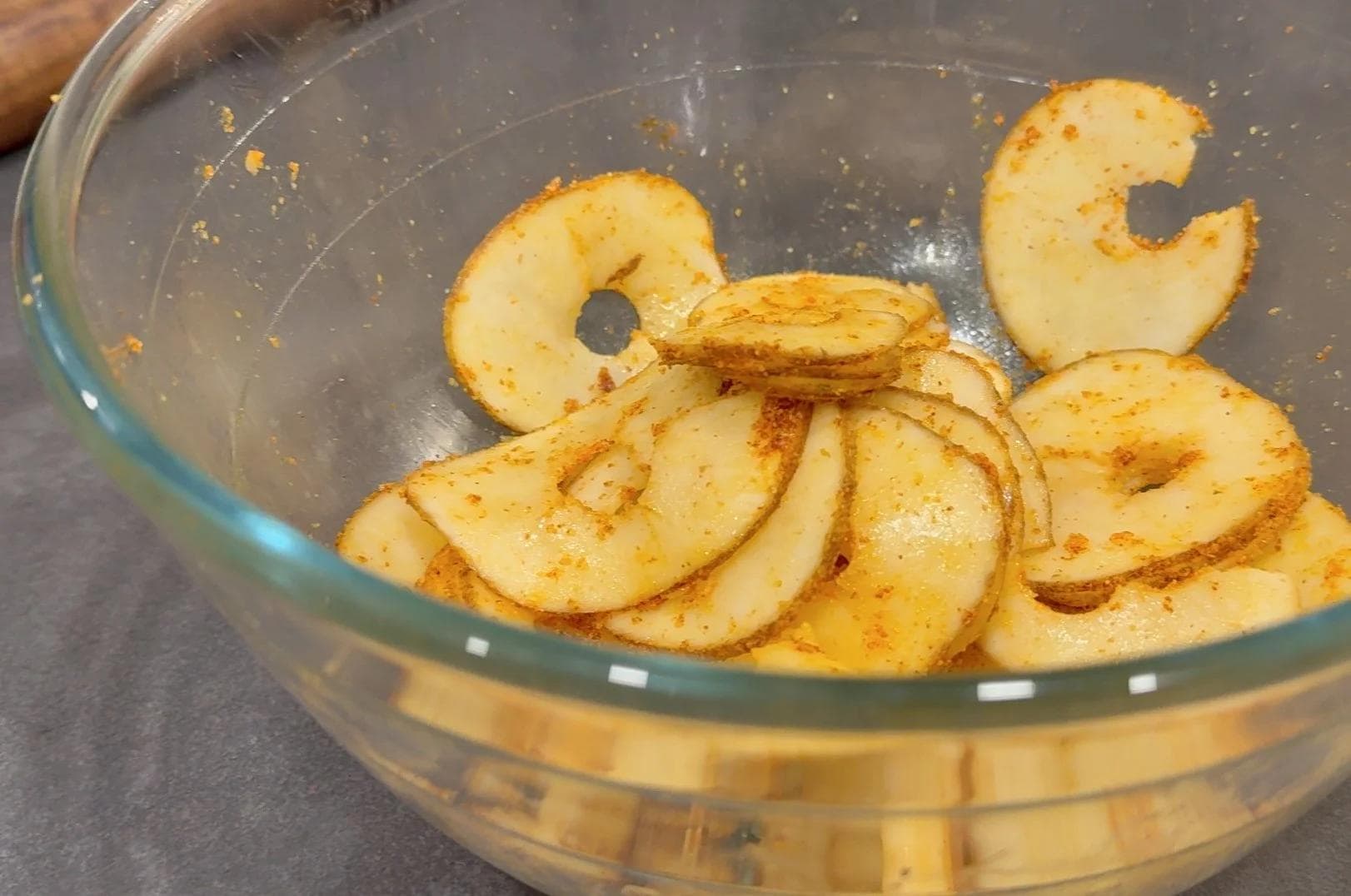 Thinly sliced potatoes seasoned with spices and butter in a glass bowl, ready for the tart assembly.