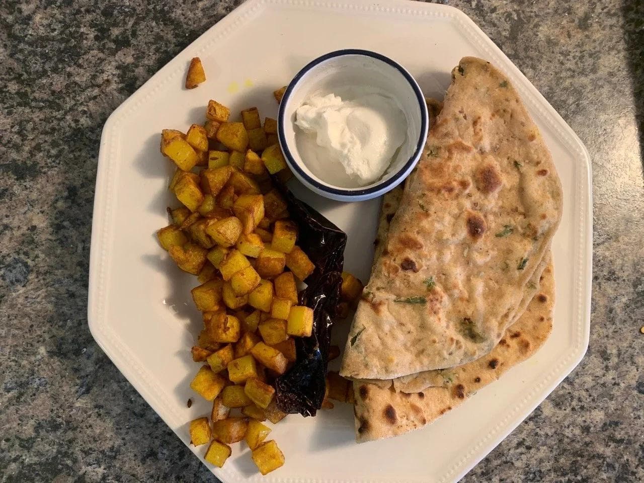 Hari mirchi paratha served with crispy golden potatoes, yogurt, and pickled vegetables on a white plate.