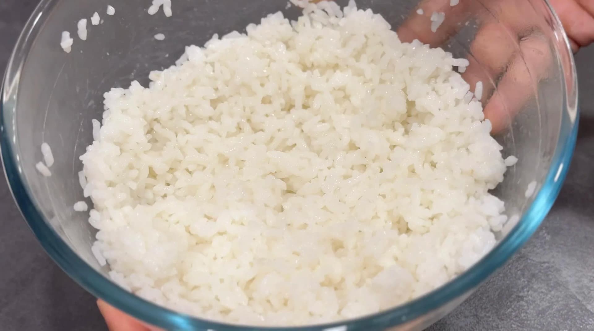 Seasoned white rice mixed with rice seasoning in a glass bowl, ready to cool before assembling the poke bowl.