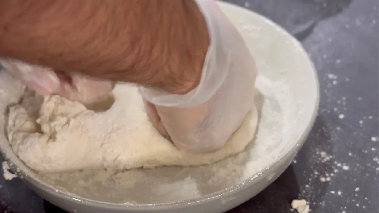 Hands kneading soft momo dough in a white bowl on a dark surface.