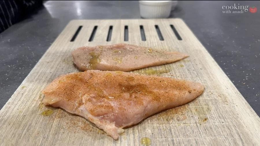 Two seasoned chicken breasts on a wooden cutting board, one with salt and pepper, one with blackening seasoning.