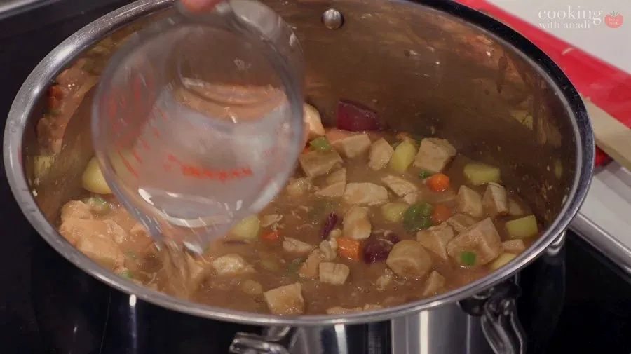 Chicken pot pie filling simmering in a pot with visible chunks of potato, carrot, peas, and chicken in a brown gravy.