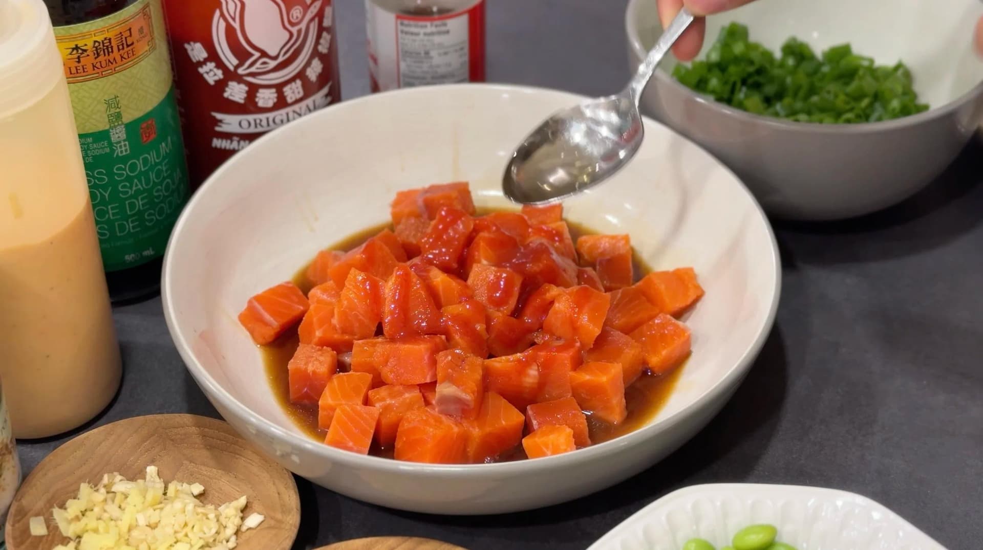 Diced salmon being mixed with soy sauce and seasonings in a white bowl with a spoon.