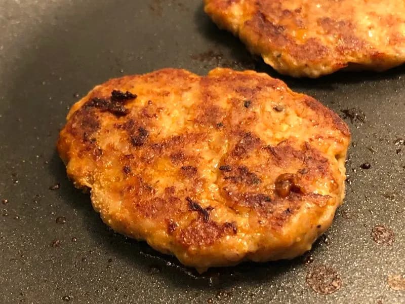 Golden-brown turkey sausage patties cooking in a skillet with a crispy, spiced surface.