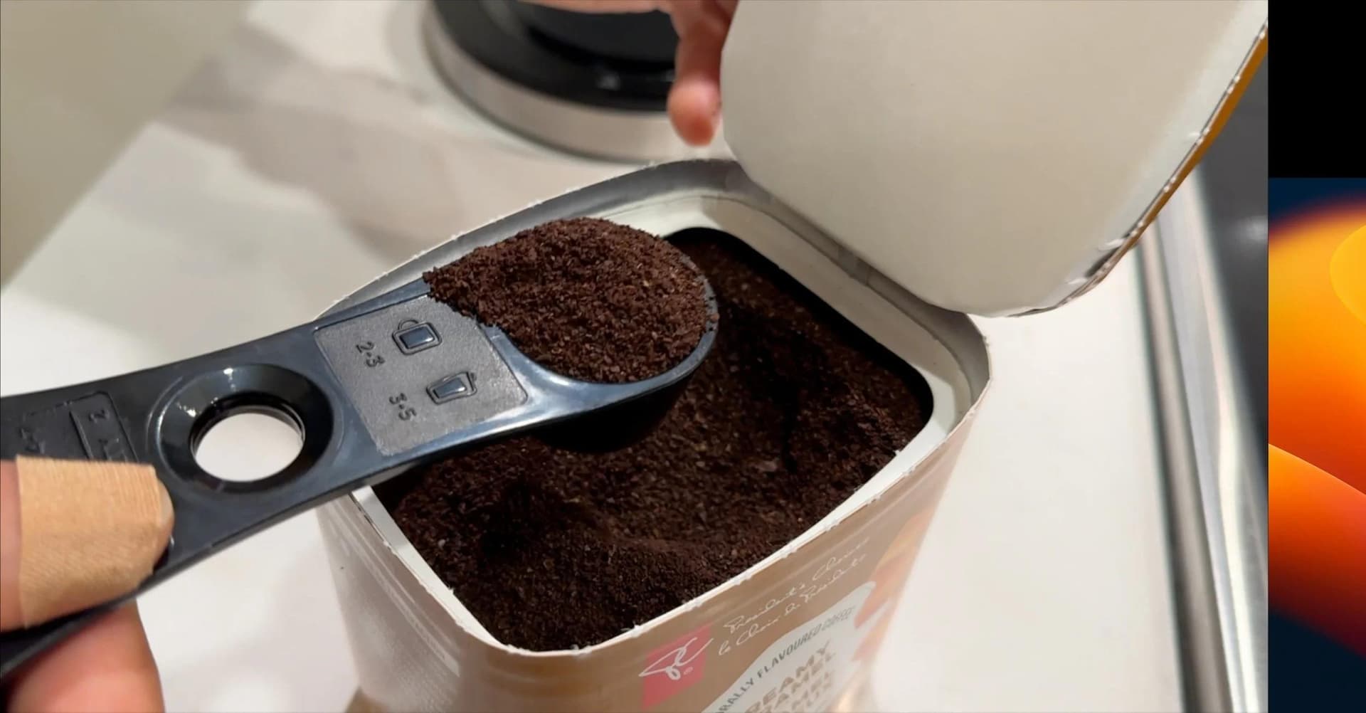 Measuring scoop of ground coffee being added to a white coffee container.